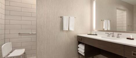 A modern bathroom with a white bathtub, a large mirror, and a vanity with a sink and towel rack.