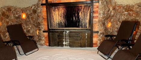 A stone-walled room with a fireplace, two chairs, and a carpet with a logo.