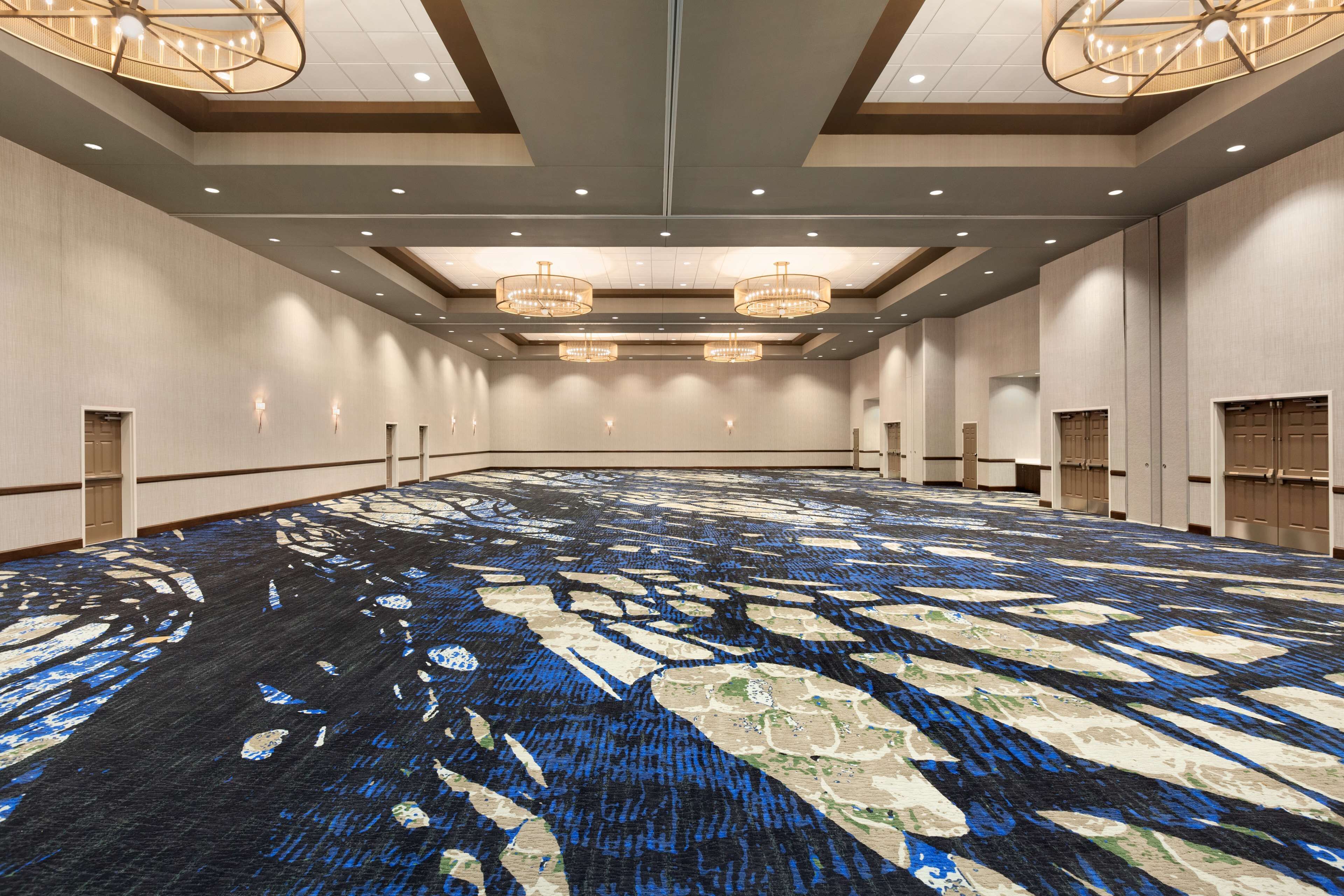 Un salón de conferencias amplio con alfombra estampada, candelabros y paneles de madera.