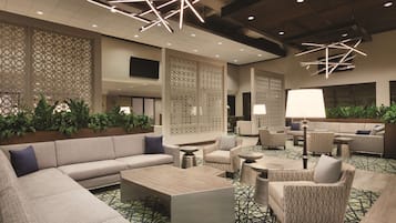 A spacious lobby with a modern design, featuring a large sofa, armchairs, a coffee table, and decorative lighting.