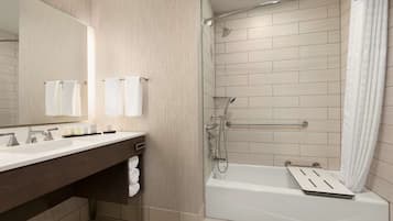 A modern bathroom with a dual sink vanity, a large mirror, a shower with a handheld showerhead, and a bathtub with a shower seat.