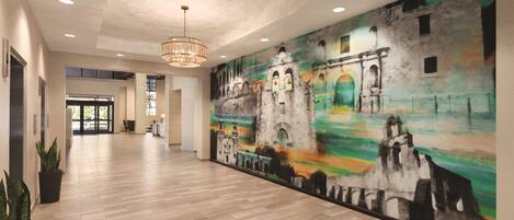 A spacious hallway with a large mural of a historical building, wooden flooring, and a chandelier.