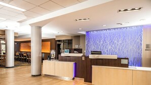 A hotel reception area with a wooden floor, a reception desk, a seating area with chairs, and a decorative wall with a tree pattern.