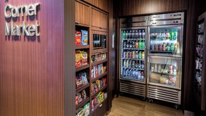 A corner market with shelves stocked with snacks and beverages, and two large refrigerators.