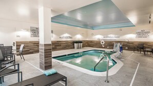 An indoor swimming pool with a tiled floor, a pool ladder, and lounge chairs.