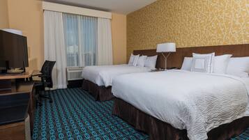 A hotel room with two beds, a desk with a chair, a TV, and a patterned carpet.