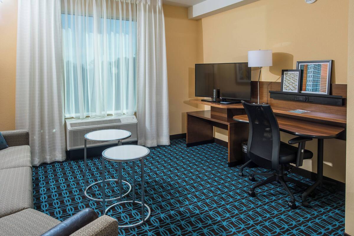 Una habitación de hotel con escritorio, silla, televisor y una pequeña mesa.