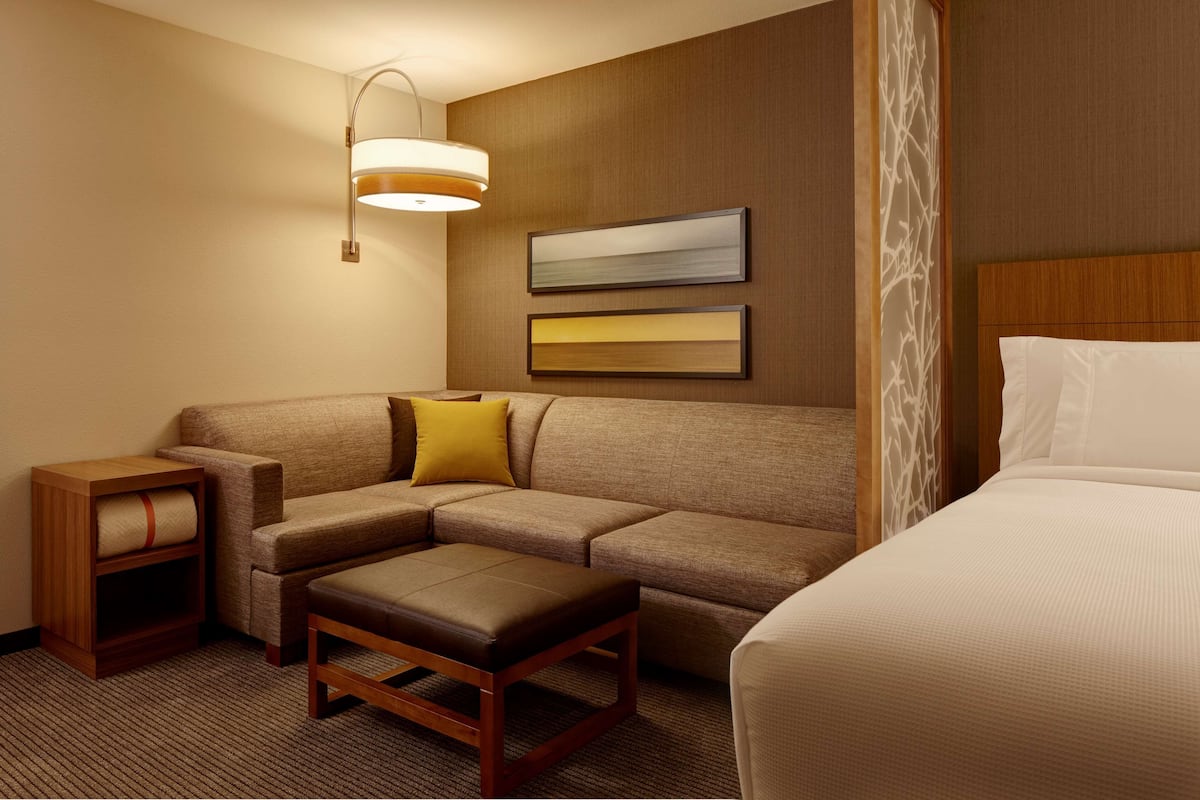 A hotel room with a sectional sofa, a wooden nightstand, a small table, and a bed.