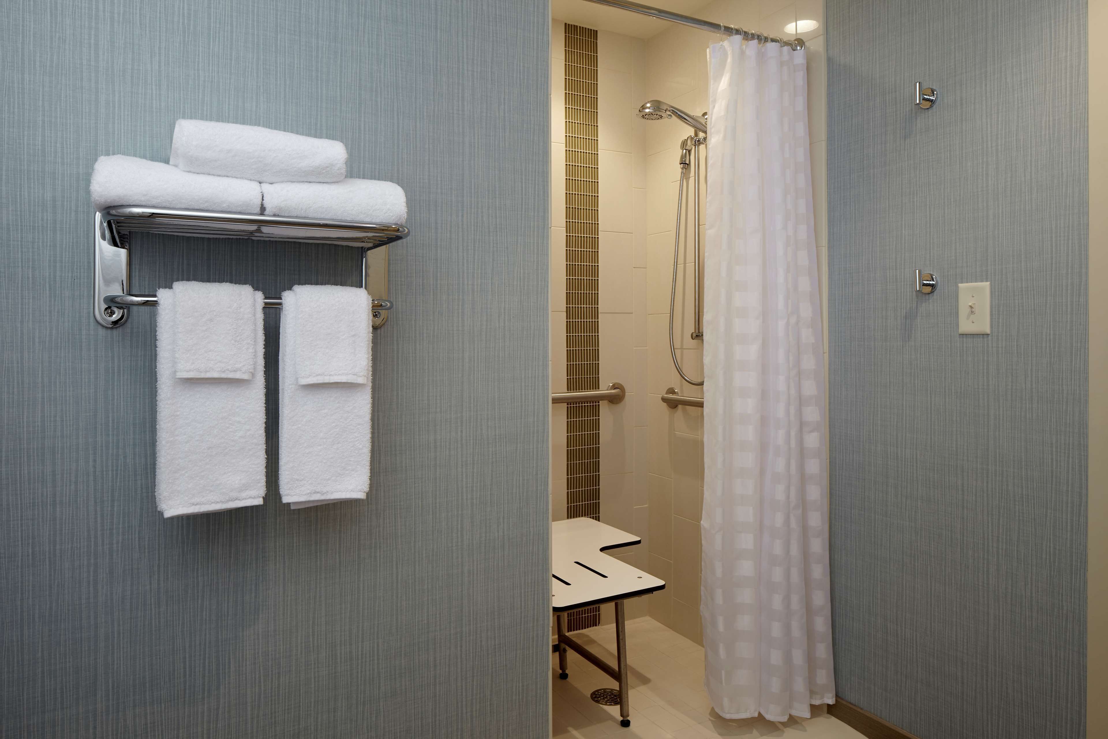 A bathroom with a towel rack holding three towels, a shower with a curtain, and a small table.