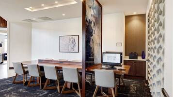 A conference room with a long table, four chairs, a computer, and a large abstract painting on the wall.