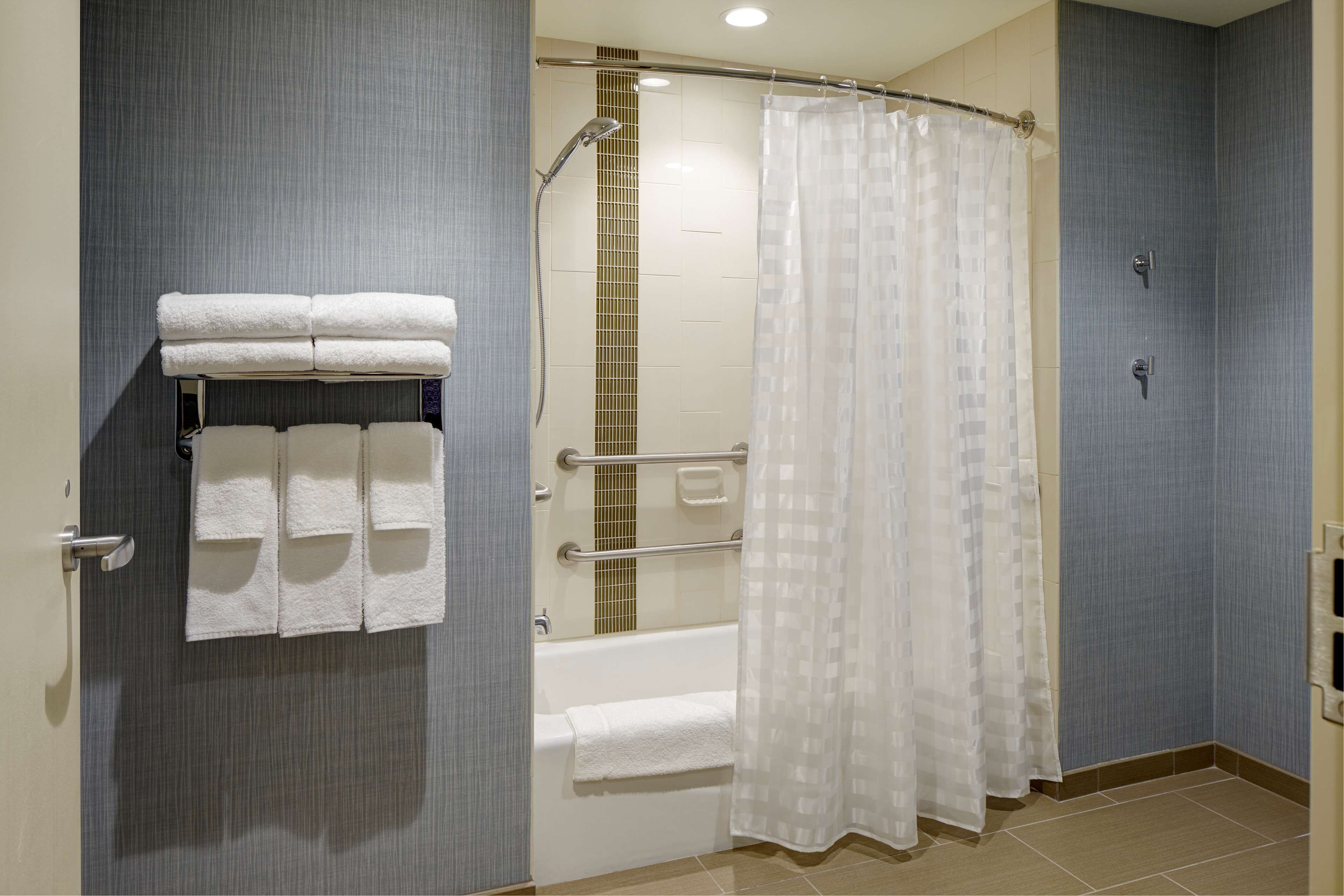 Een moderne badkamer met een douche, een bad en een handdoekrek met opgevouwen handdoeken.
