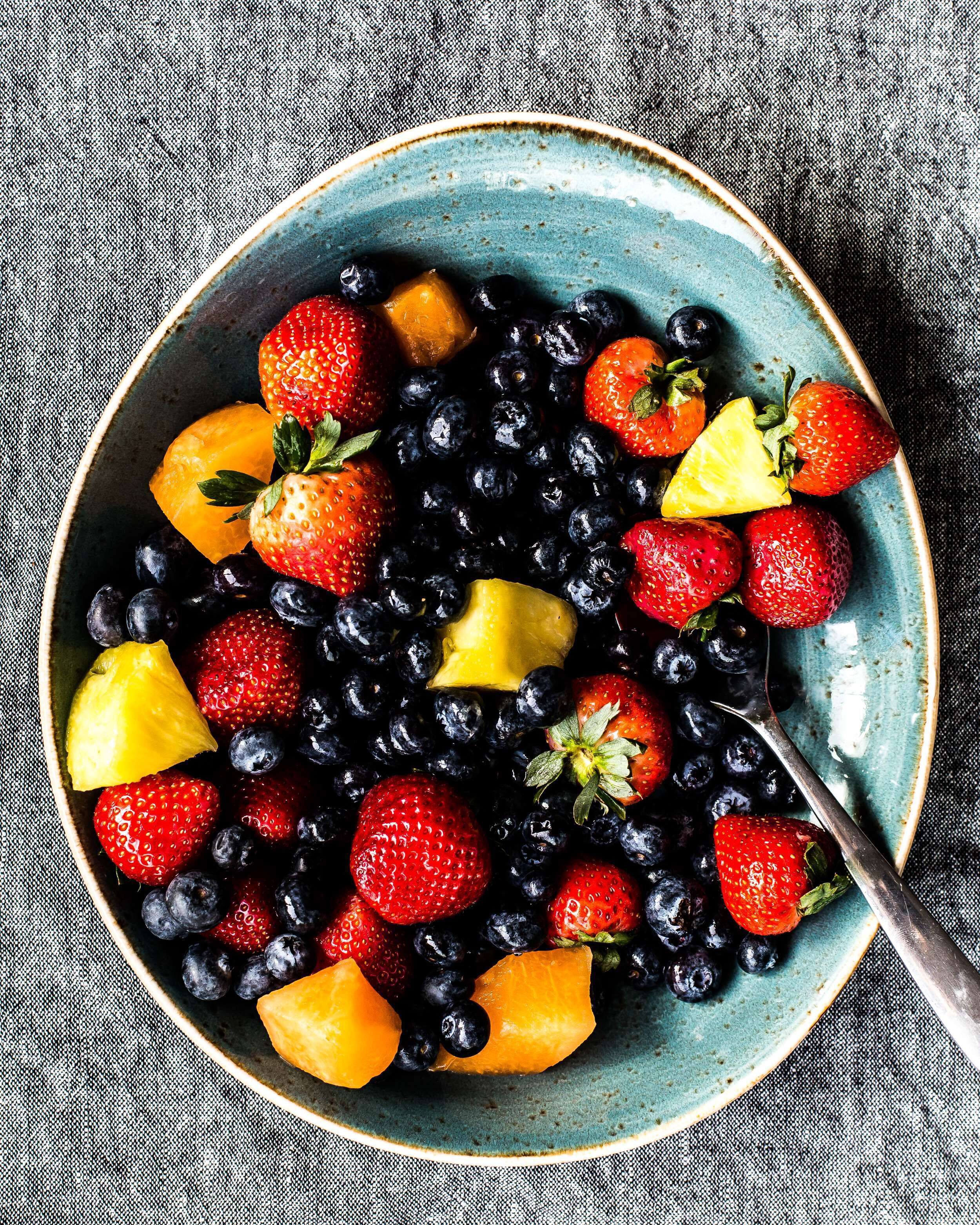 A bowl of mixed fruits including strawberries, blueberries, and pineapple chunks.