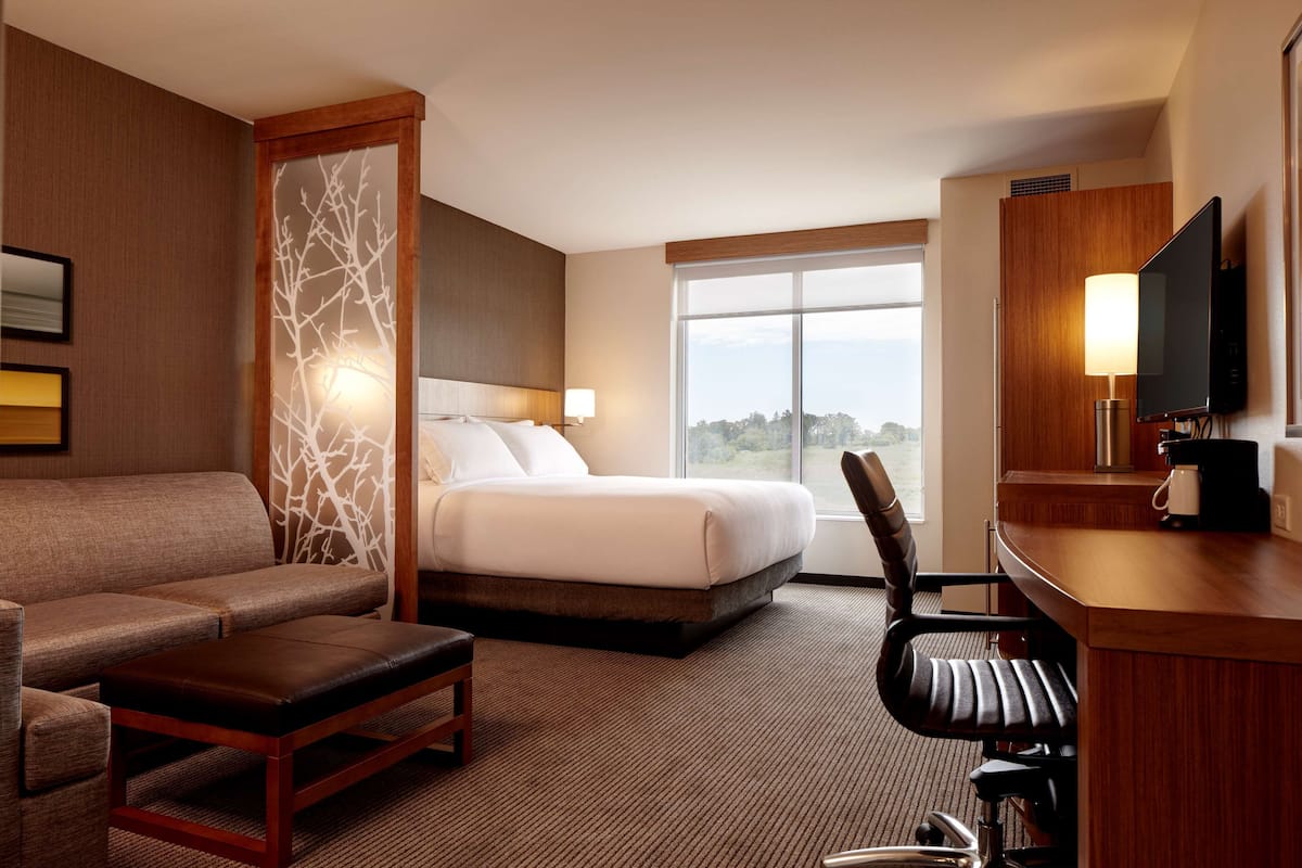 A hotel room with a bed, a sofa, a desk with a TV, and a large window.