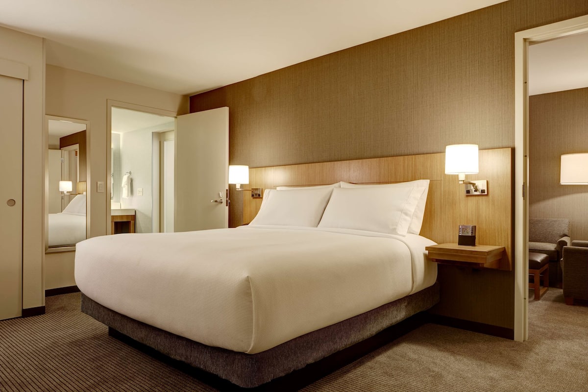 A hotel room with a large bed, bedside tables with lamps, a mirror, and a door leading to another room.