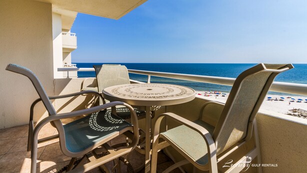 A balcony with a round table and four chairs, overlooking a beach with umbrellas and people. - Perdido Sun 816 (Pensacola)