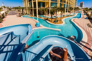 Área de parque aquático com piscina, toboáguas e um edifício ao fundo.
