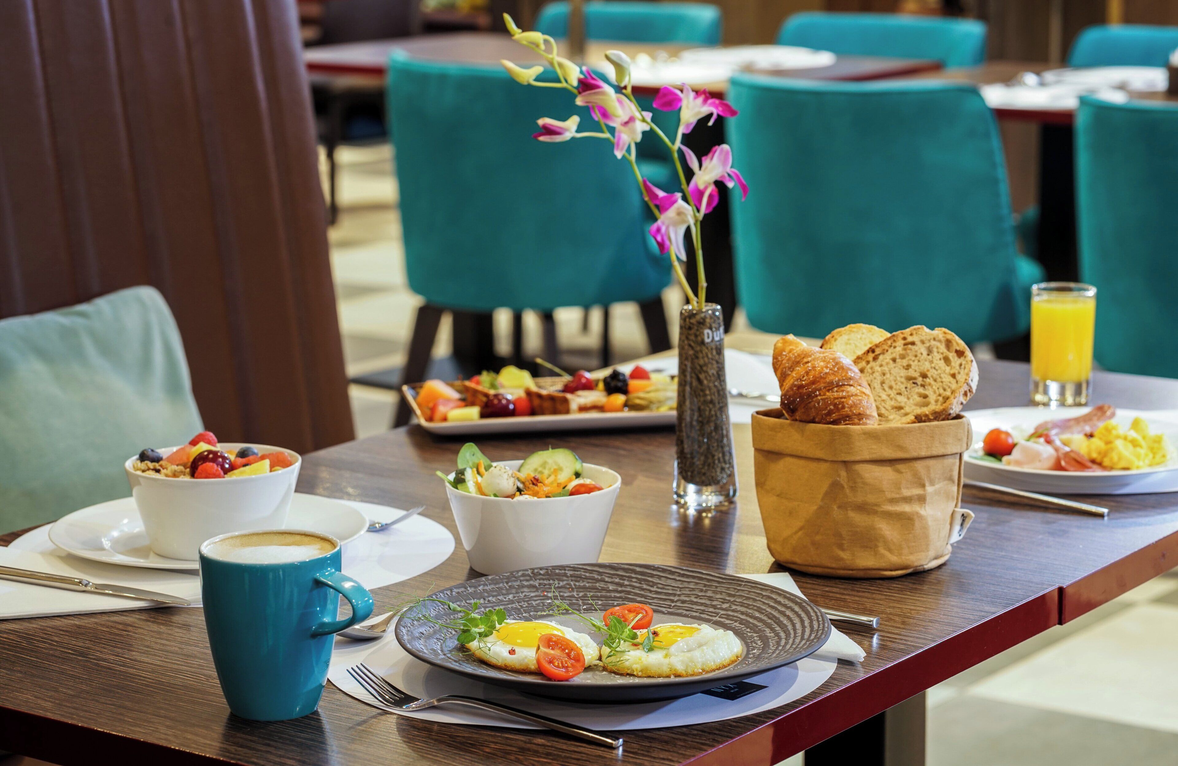 Une table en bois dressée pour le petit-déjeuner, avec une tasse de café, une assiette d’œufs, un panier de fruits et un panier de pain.