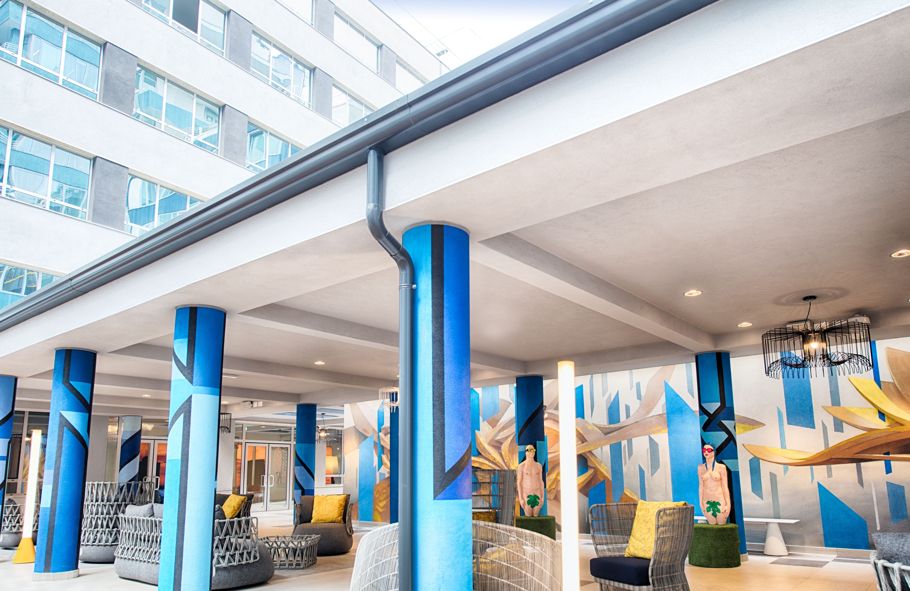 A modern hotel lobby with geometric wall art, blue and white pillars, and comfortable seating areas.