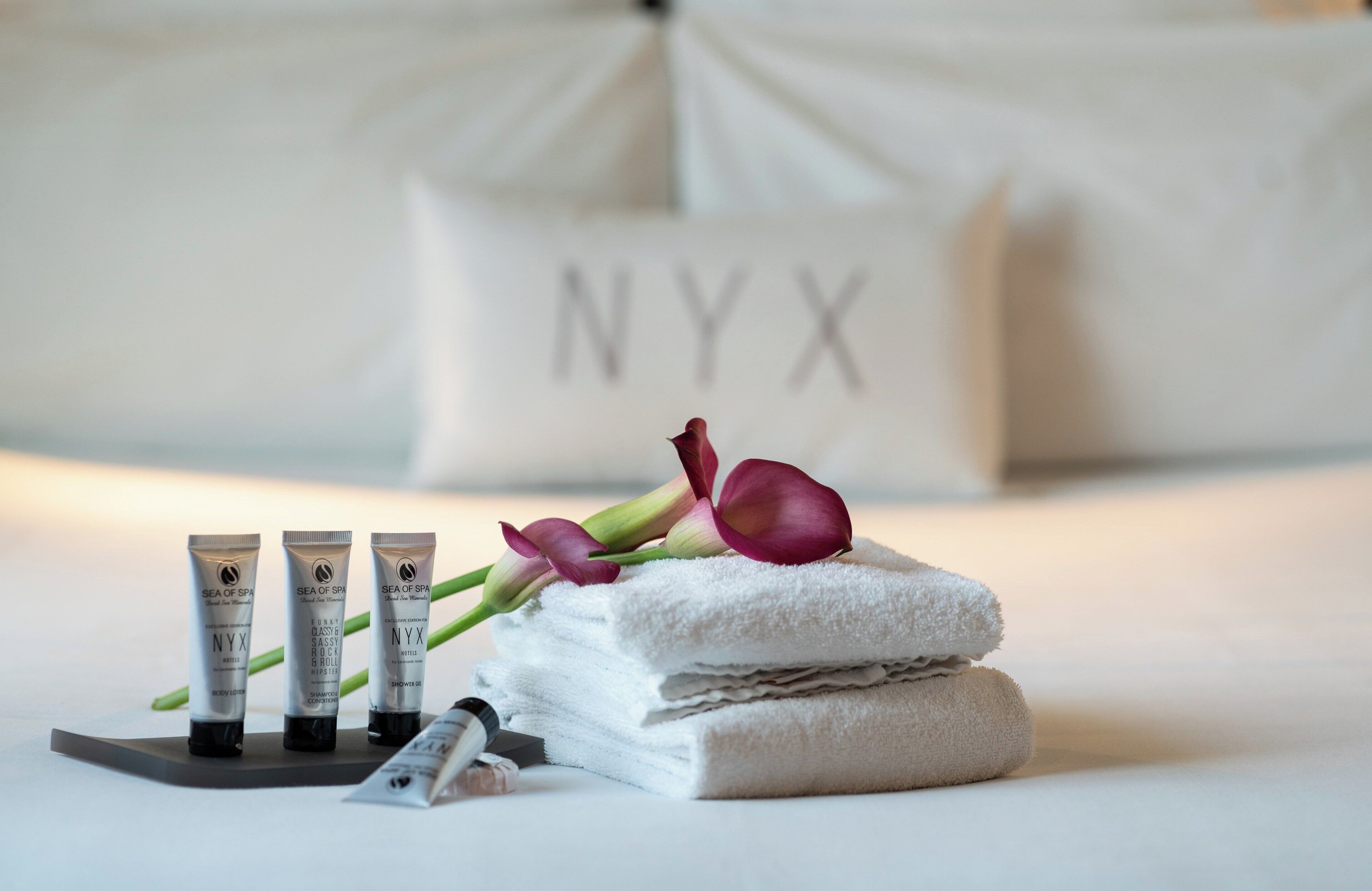 Een netjes gerangschikte verzorgingsset op een dienblad, met body lotion, shampoo, conditioner en douchegel, en een handdoek en bloem erbovenop.