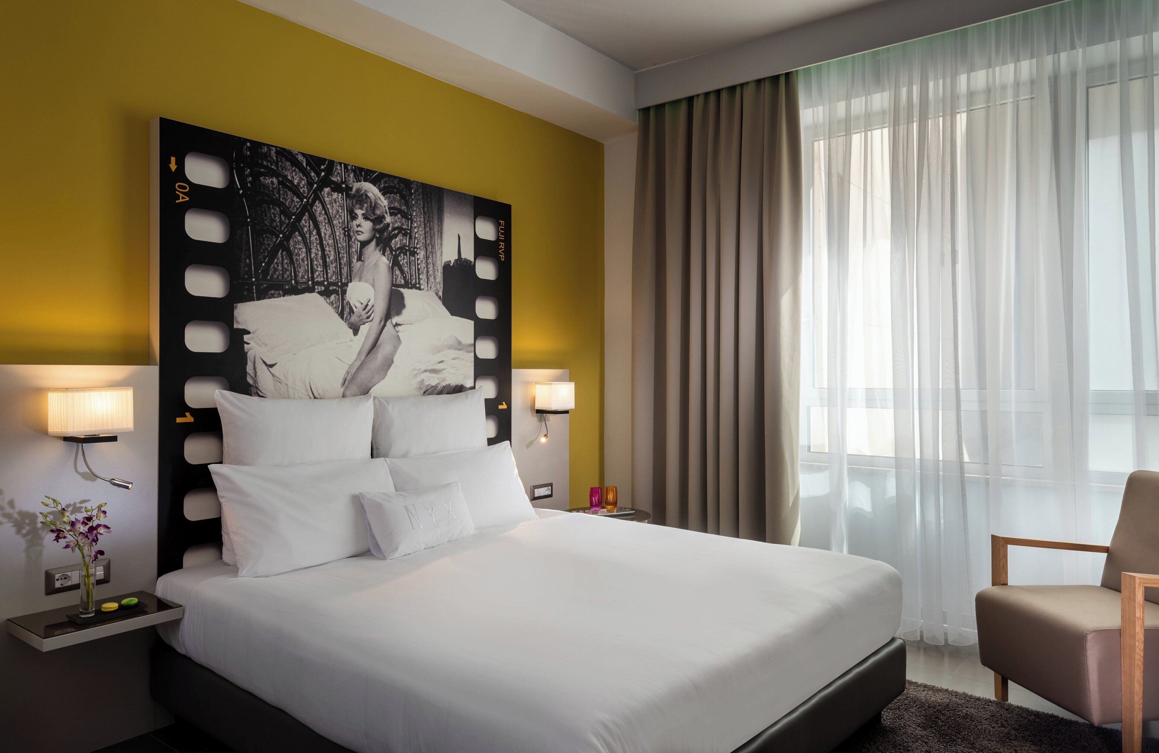A hotel room with a large bed, two bedside lamps, a nightstand with a vase of flowers, and a large framed picture on the wall.