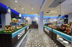 A modern buffet with a variety of fruits and pastries, a patterned floor, and ambient lighting. - NYX Hotel Milan by Leonardo Hotels (Milan)