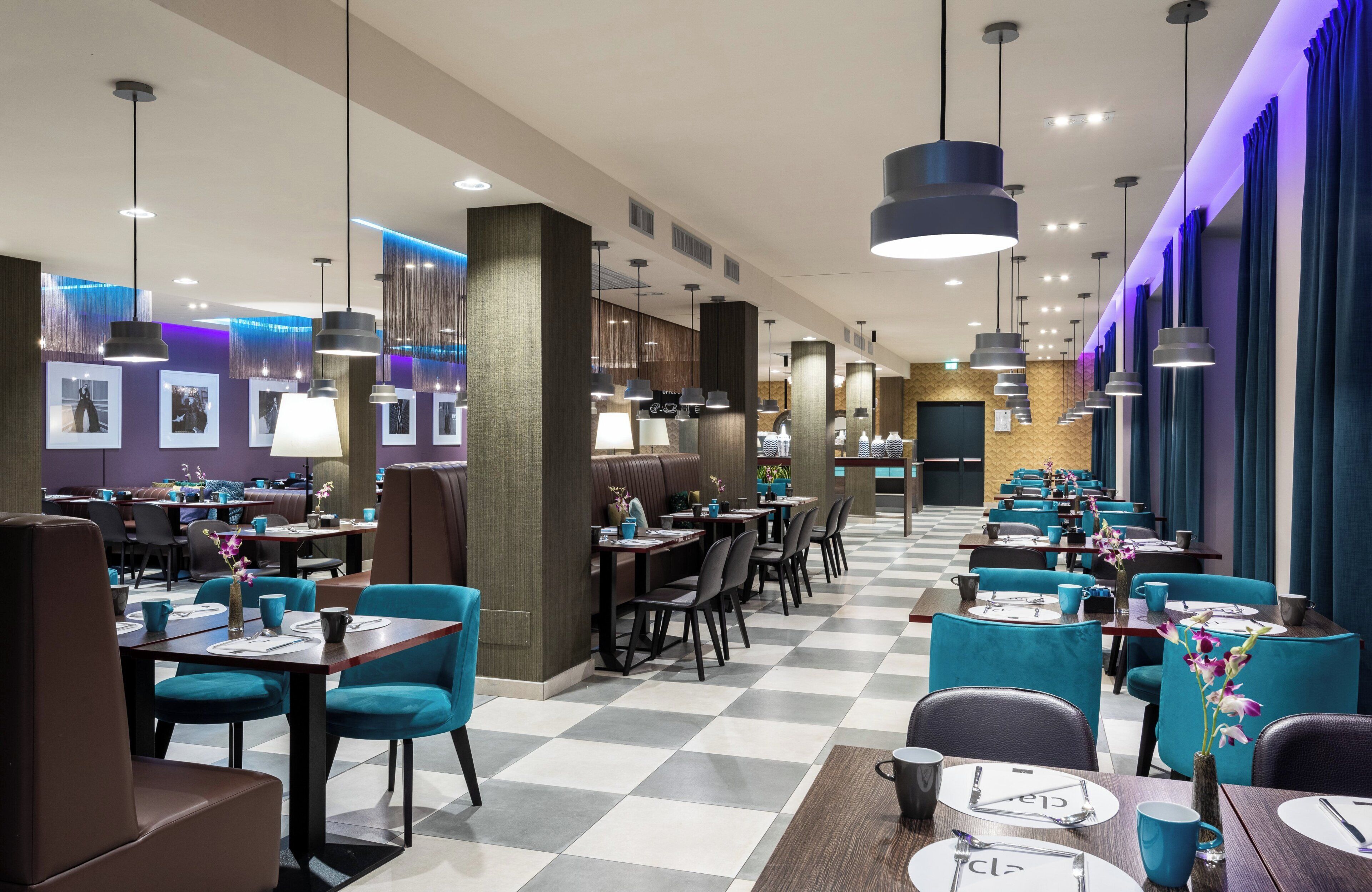 A modern restaurant with checkered flooring, teal chairs, and pendant lighting.
