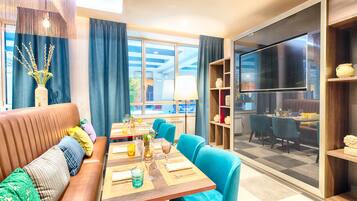 A modern dining area with a wooden table, blue chairs, and a sofa with cushions.