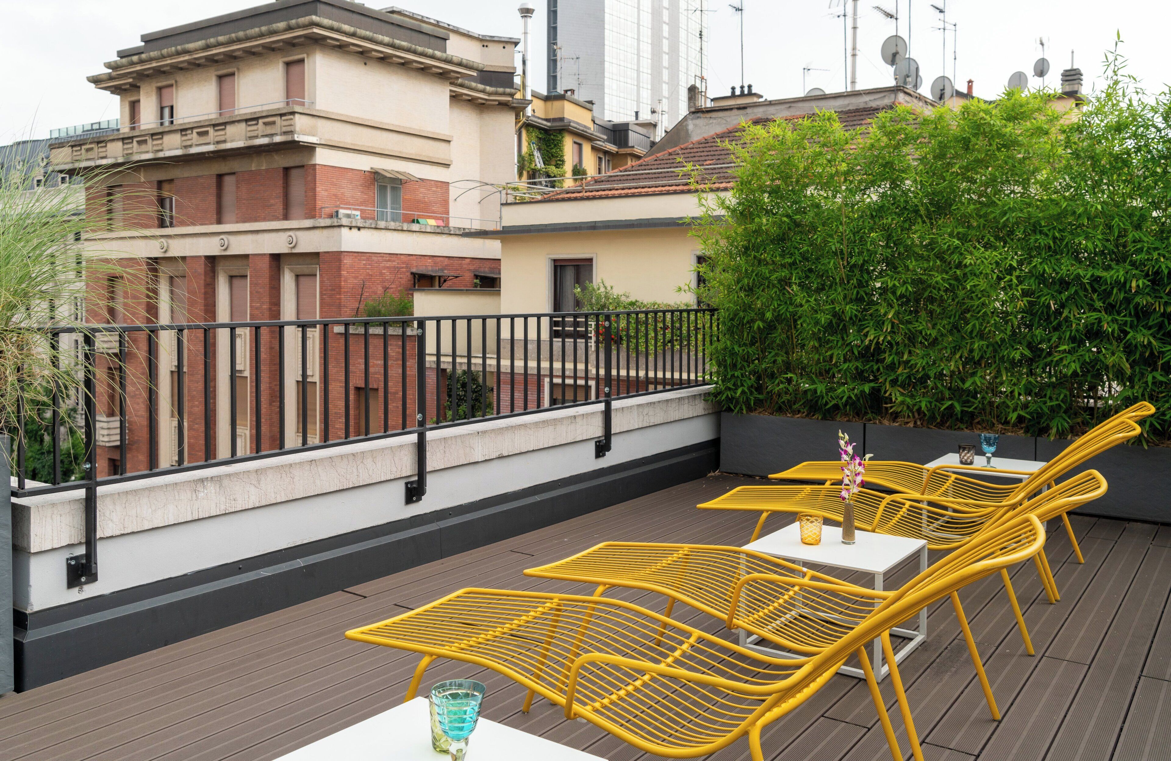 A rooftop terrace with yellow metal chairs and tables, surrounded by a black metal railing.