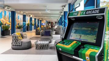 A modern arcade area with a neon sign reading "The NYX Arcade," featuring a classic arcade machine and contemporary seating.