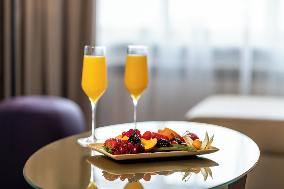 Una mesa con una bandeja de fruta y dos vasos de zumo de naranja en una habitación de hotel moderna.