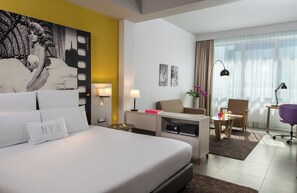 A hotel room with a large bed, a desk, a chair, a small table with a lamp, and a window with curtains. - NYX Hotel Milan by Leonardo Hotels (Milan)