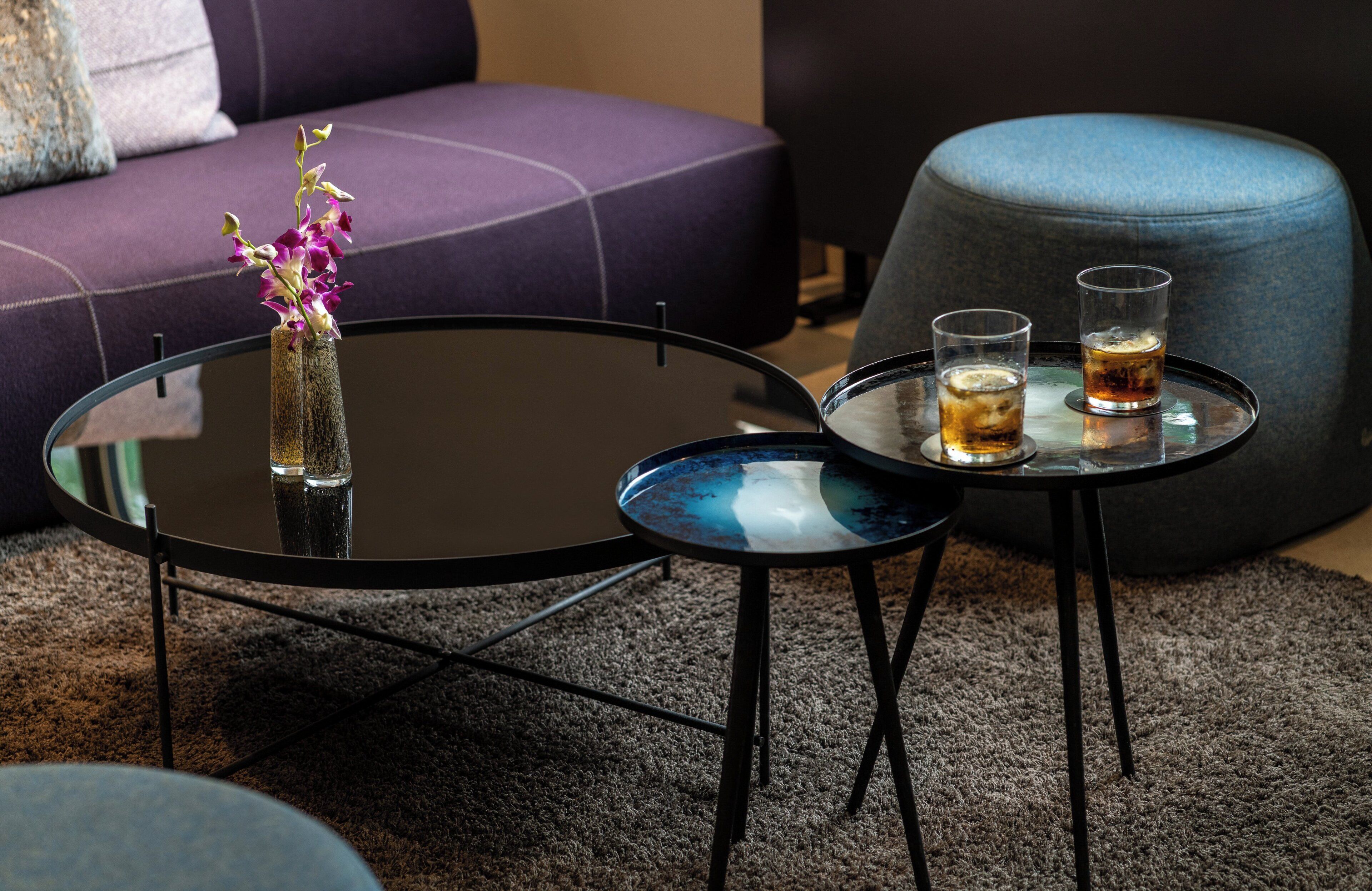 Un salon moderne avec une table basse ronde en verre, une petite table d’appoint et un canapé violet.