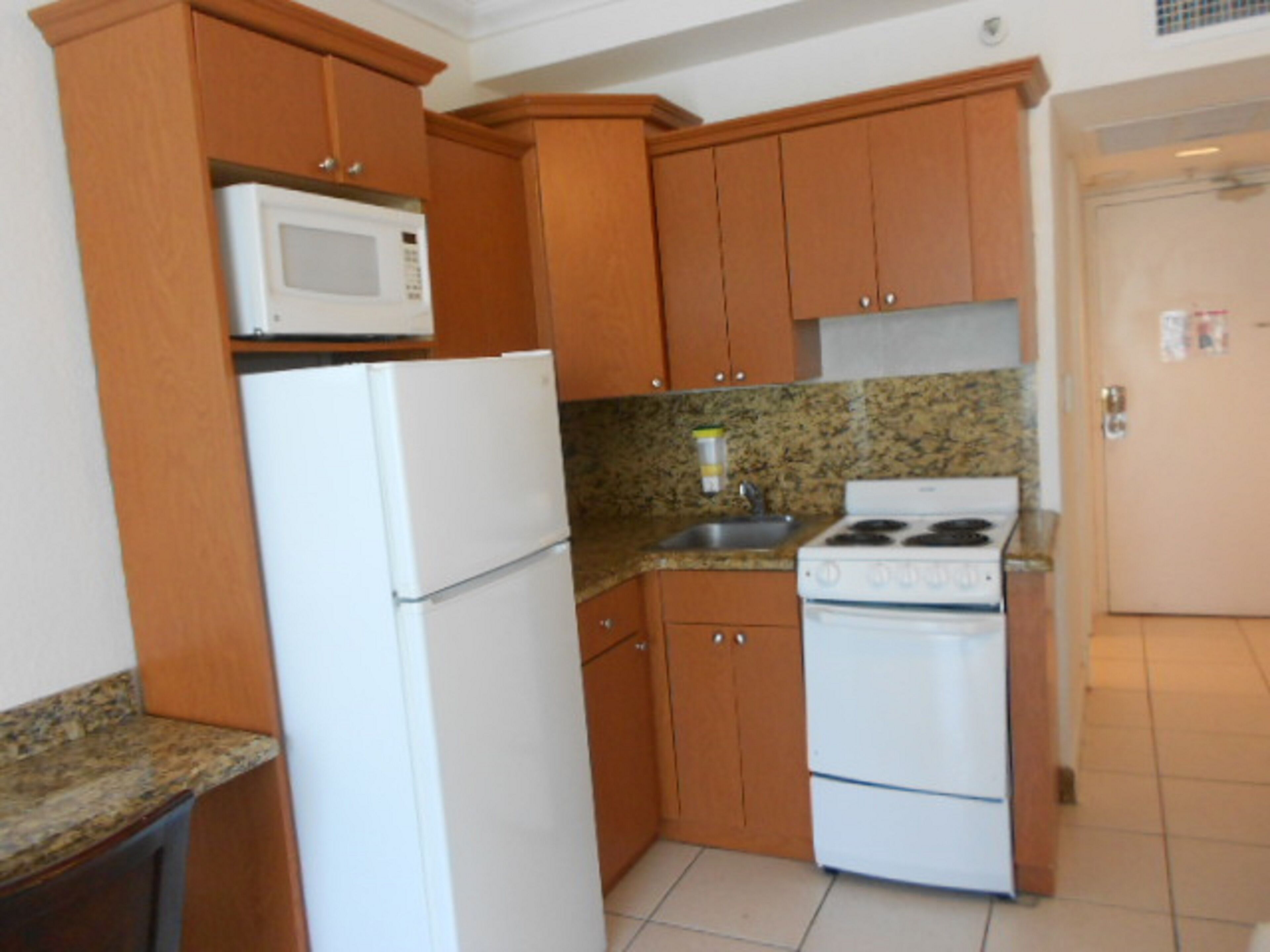 A compact kitchen with wooden cabinets, a white refrigerator, a microwave, and a stove.