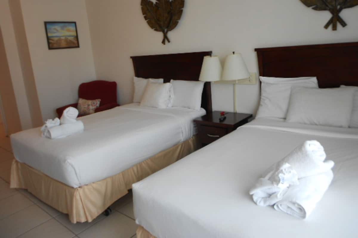 Une chambre d’hôtel avec deux lits, une table de chevet, une lampe et un élément décoratif en forme de feuille fixé au mur.