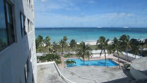 Vista de una playa con piscina, palmeras y un crucero en la distancia.