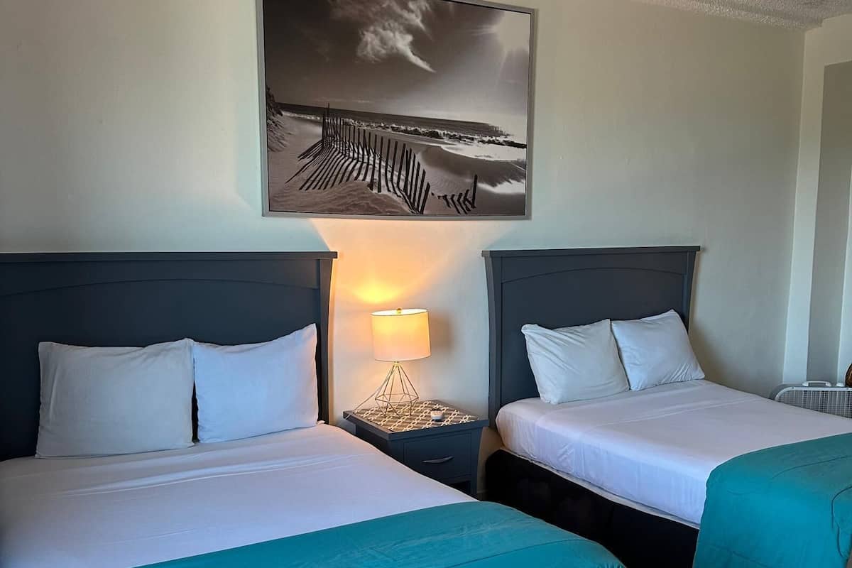 Une chambre d’hôtel avec deux lits, une table de chevet avec une lampe et un tableau encadré au mur.