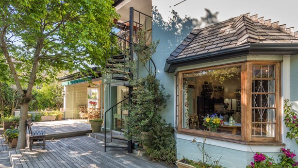 A wooden deck with a bench, a small building with a window displaying flowers, and a staircase leading to an upper level. - Hedge House (Cape Town)