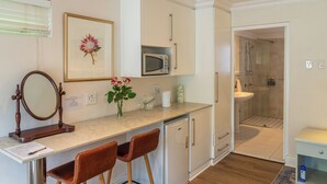 A compact kitchen with a microwave, a sink, and a refrigerator. There are two chairs and a small table with a mirror. - Hedge House (Cape Town)