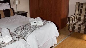 A hotel room with a large bed, a wardrobe, a chair, and a ceiling fan. - Ebony and Ivory (Bloemfontein)
