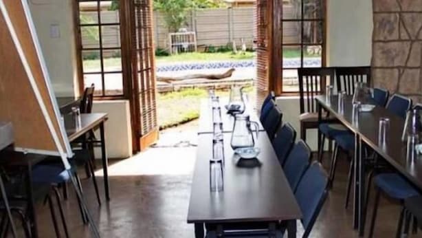 A dining area with a long table and chairs, a stone wall, and a view of a garden with a bird. - Ebony and Ivory (Bloemfontein)