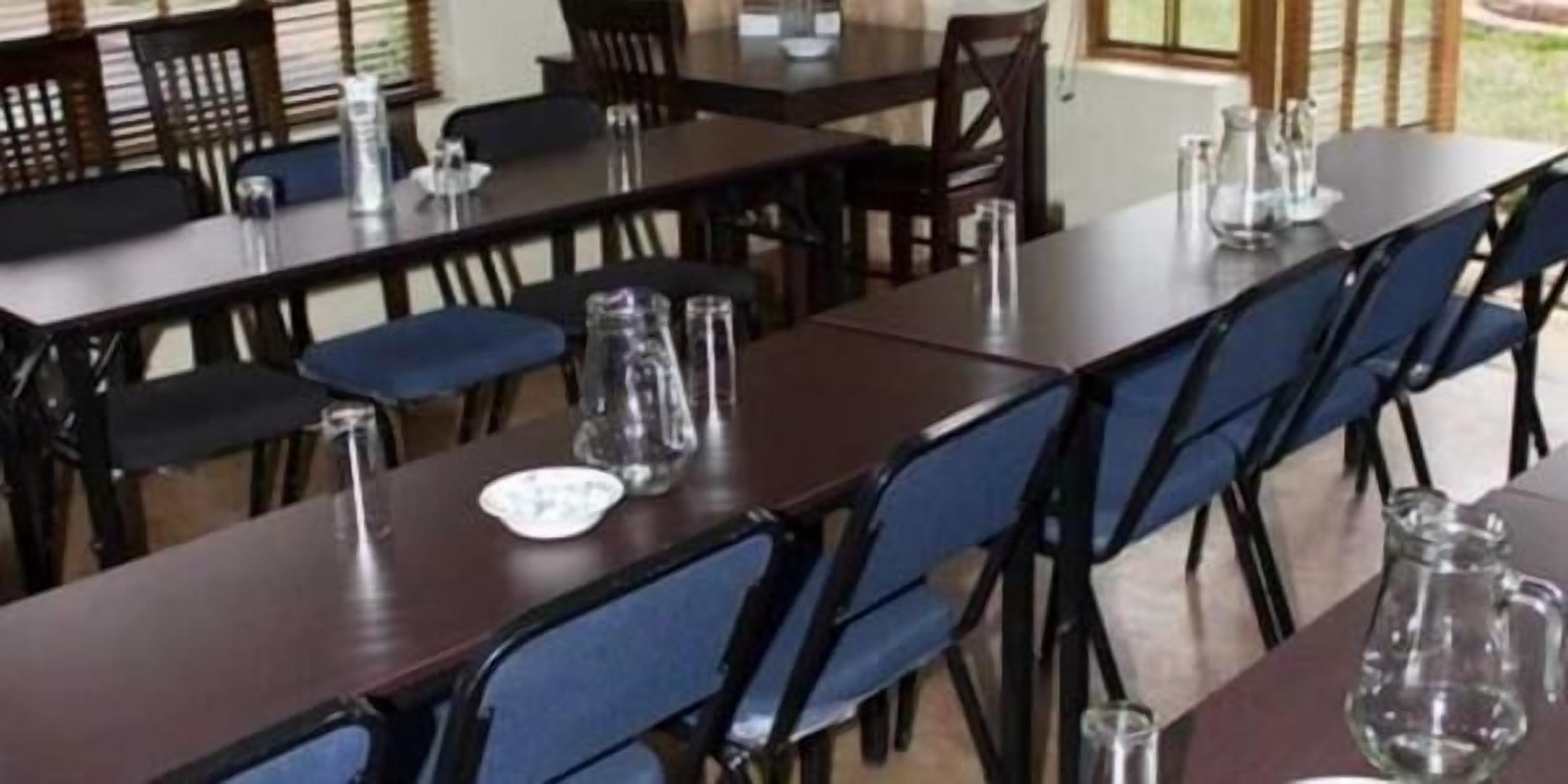 Un comedor con mesas largas y sillas azules, equipado con vasos de agua y platos.