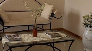 A living room with a sofa, a coffee table with magazines, a vase with flowers, and a decorative wall piece. - Ebony and Ivory (Bloemfontein)