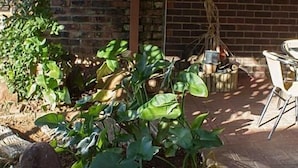 A patio area with a brick wall, a table and chairs, and various potted plants. - Ebony and Ivory (Bloemfontein)