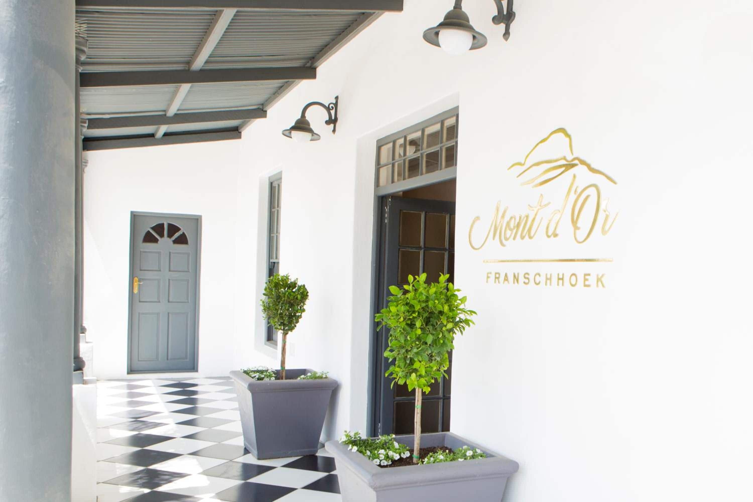 L’entrée d’un hôtel avec un sol à carreaux, une porte grise et des plantes en pot.