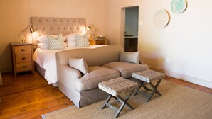 A bedroom with a large bed, a sofa, two wicker side tables, and a nightstand with a lamp. - Mont d'Or Franschhoek (Franschhoek)