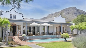 A modern house with a swimming pool, outdoor seating, and a mountain backdrop. - Mont d'Or Franschhoek (Franschhoek)