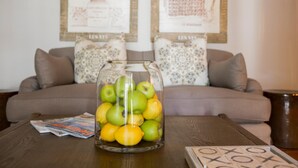 A glass jar filled with apples and lemons on a wooden table, with a magazine and a tic-tac-toe game in front of a sofa with patterned cushions. - Mont d'Or Franschhoek (Franschhoek)