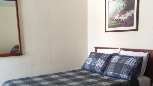 A single bed with a plaid bedspread, a headboard, and a nightstand with a lamp.