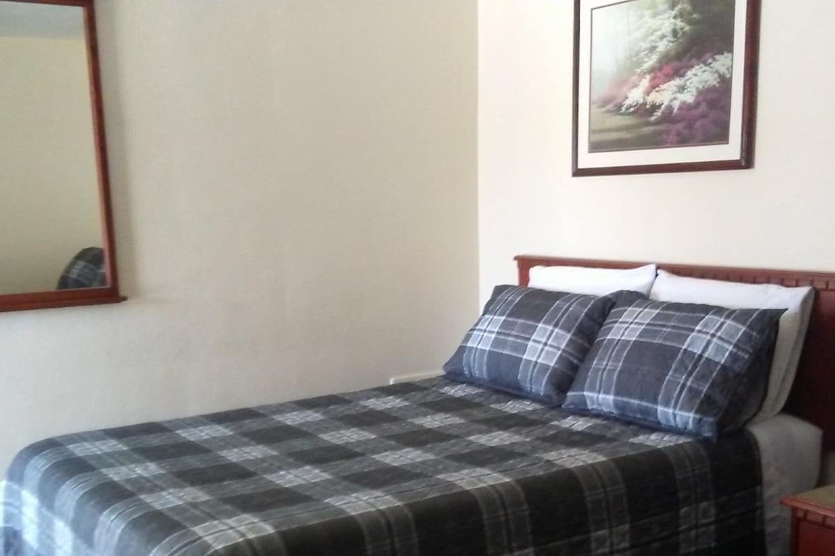 A single bed with a plaid bedspread, a headboard, and a nightstand with a lamp.