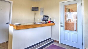 A reception desk with a computer, a flat-screen TV, and a small shelf with items. There is a door to the right and a white door to the left.
